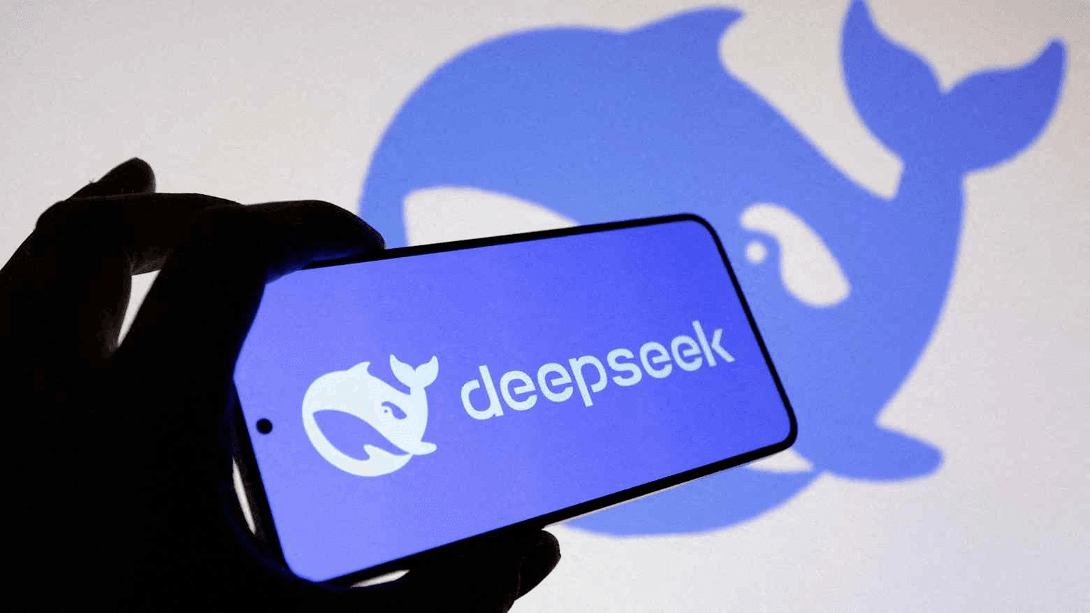 DeepSeek logo on a phone held in front of a blue whale logo projection